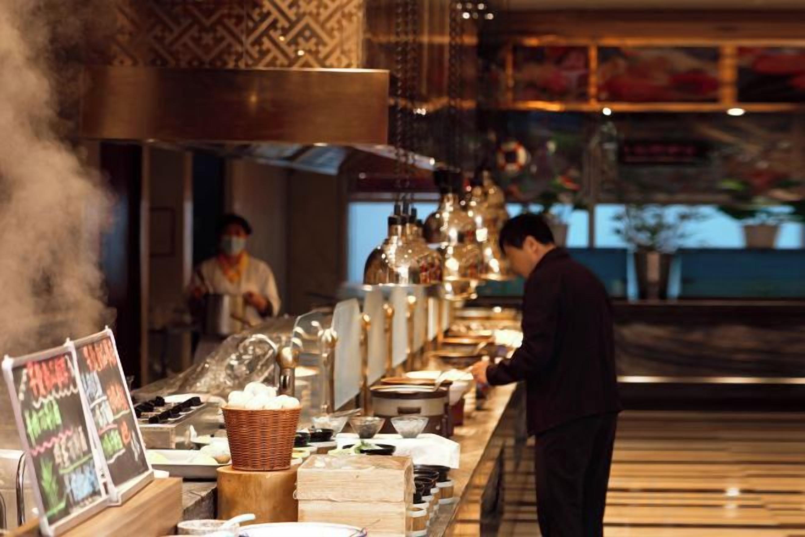 A restaurant interior with a long counter, steam rising from the stove, and a person working in the background.