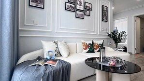 A modern living room with a white sofa, a black coffee table, and framed pictures on the wall. - Center-Beachfront Breeze Apt–2BR-3 beds- Fast WiFi (Nha Trang)