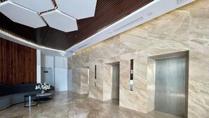 A modern lobby with a marble floor, wooden paneling, a sofa, a coffee table, and three elevators. - Center-Beachfront Breeze Apt–2BR-3 beds- Fast WiFi (Nha Trang)