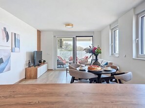 Ett modernt vardagsrum med en matplats, en TV och ett stort fönster.