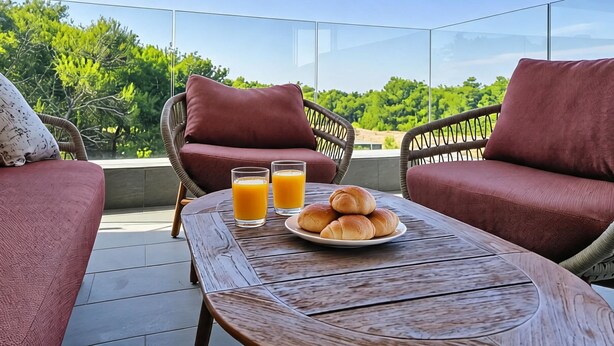A balcony with wicker furniture, a wooden table, and a plate of bread and juice. - Apartment Karlo by Interhome (Pag/Povljana)