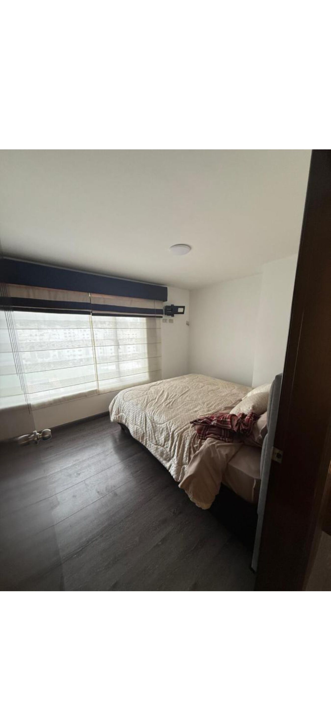 Un dormitorio con una cama, una ventana con persianas, una lámpara de techo y una puerta.