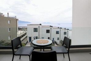 A balcony with a round table and two chairs, overlooking a sea and buildings. - Velaris Apartment 202 (Vlorë)