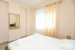 A hotel room with a bed, a bedside table, a mirror, and a window with curtains. - Velaris Apartment 202 (Vlorë)
