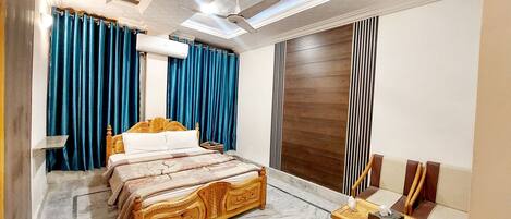A bedroom with a wooden bed, blue curtains, an air conditioning unit, and a ceiling fan.