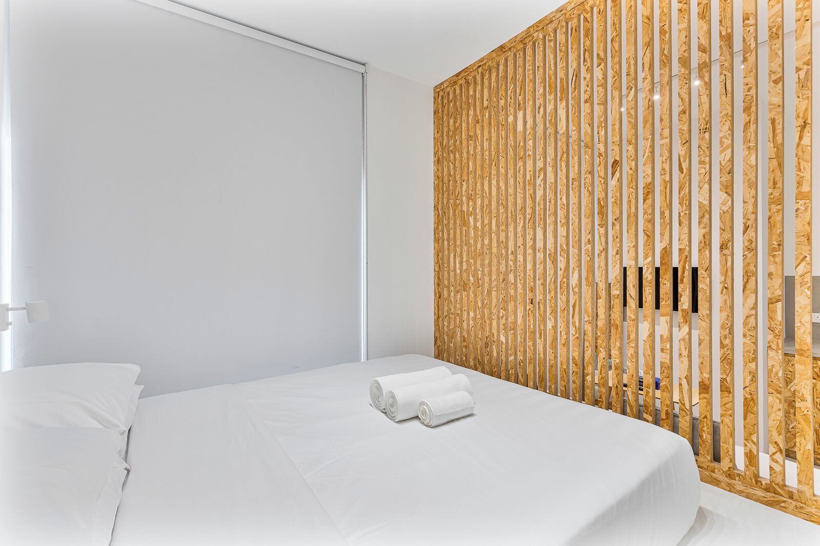 A modern hotel room with a large bed, white linens, a wooden slatted wall, and a window.