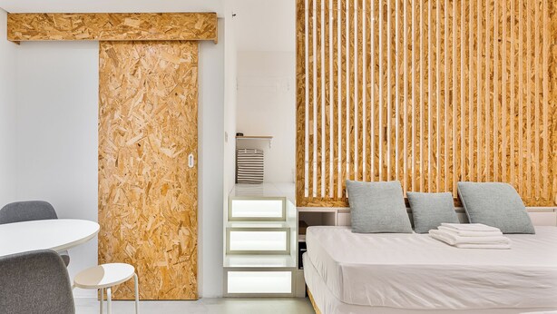 Un dormitorio moderno con cama, mesitas de noche, una silla y un panel de pared de madera.