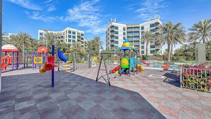 Un parque infantil con diversas estructuras de juego, una zona pavimentada y un edificio al fondo.