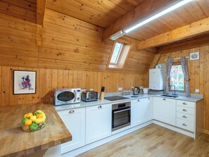 A wooden-paneled kitchen with a microwave, toaster, sink, oven, and a fruit bowl on the counter. - Birch Rowan Combi by Interhome (Drumnadrochit)