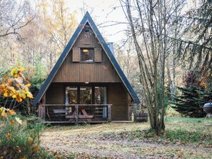 Une cabane dotée d’un toit triangulaire, de grandes fenêtres et d’une terrasse en bois.