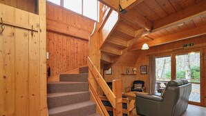 Ein Holzinnenraum mit Treppe, einer Couch und Blick auf den Wald.
