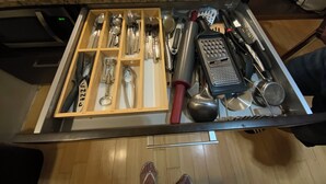 Un cajón con utensilios de cocina, un rallador y una taza de café sobre una encimera de granito.