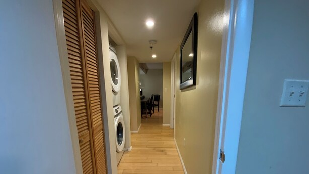 Un pasillo con suelo de madera, una lavadora y un cuadro enmarcado en la pared.