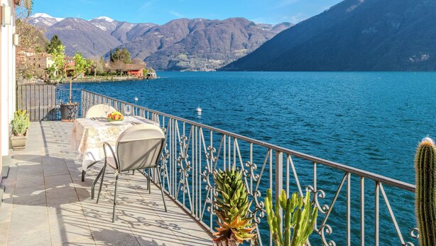 Eine Terrasse mit Tisch und Stühlen mit Blick auf einen See, im Hintergrund Berge.