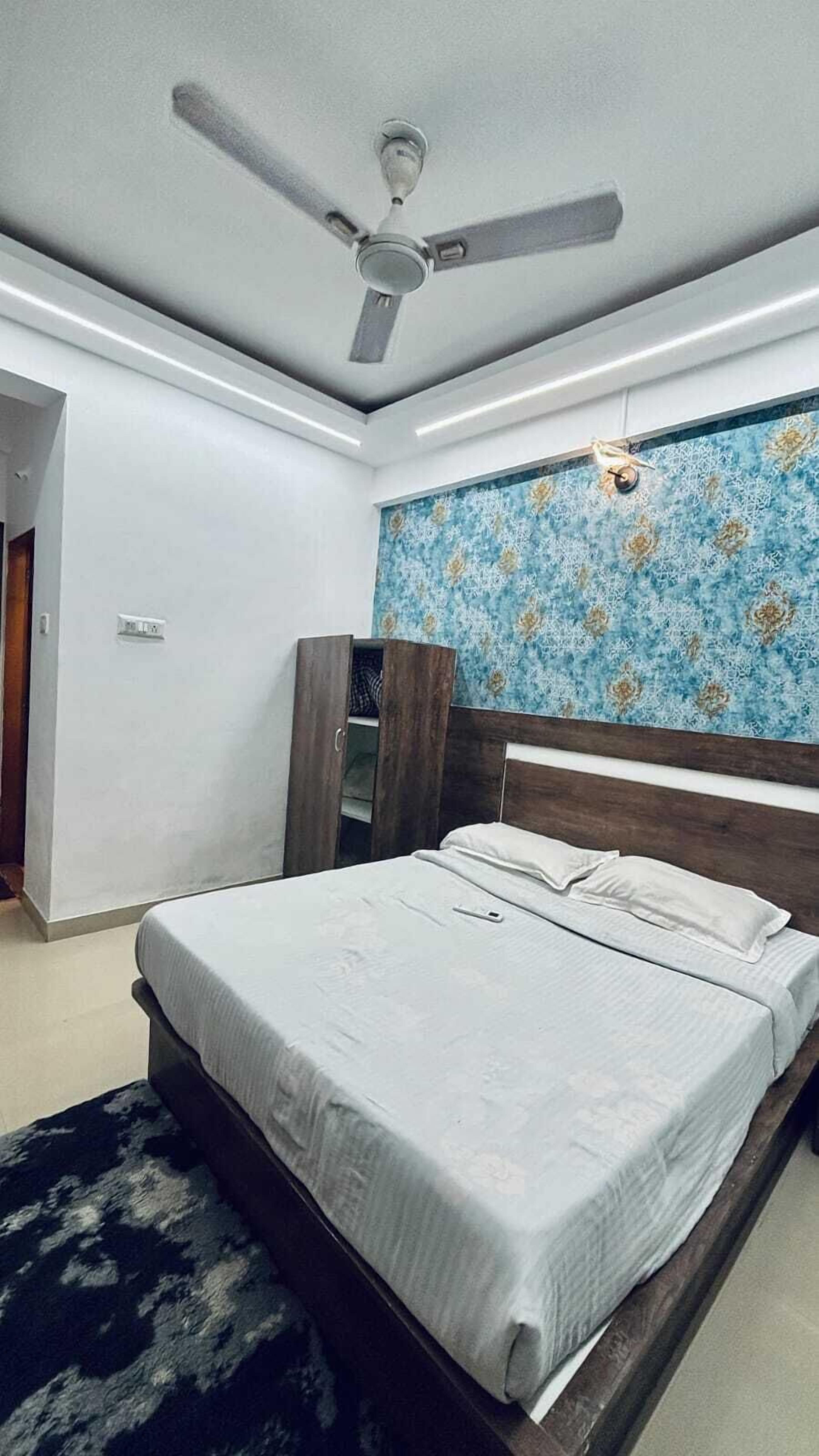 Een slaapkamer met een bed, een plafondventilator, een kledingkast en een behang met een patroon.