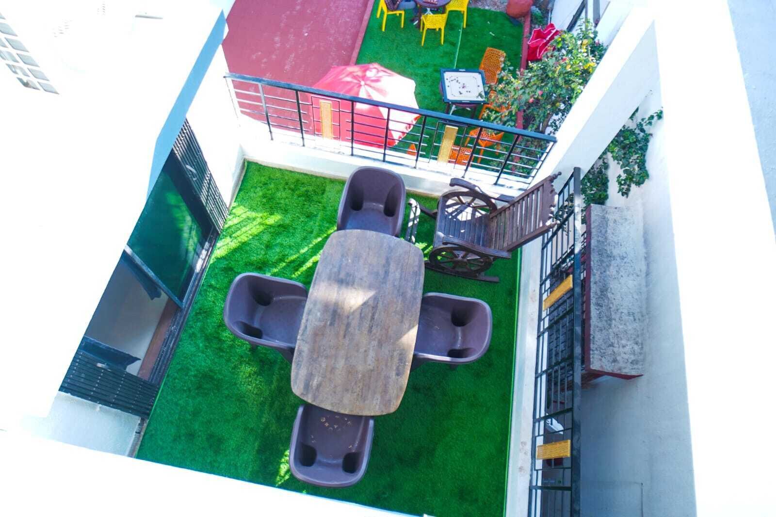 Eine Dachterrasse mit Holztisch und vier Stühlen, umgeben von einer grünen Rasenfläche und einem roten Spielbereich.