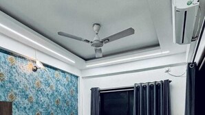 A bedroom with a bed, a ceiling fan, a window with curtains, and an air conditioning unit. - Ananya Holidays Villa (Lonavala)