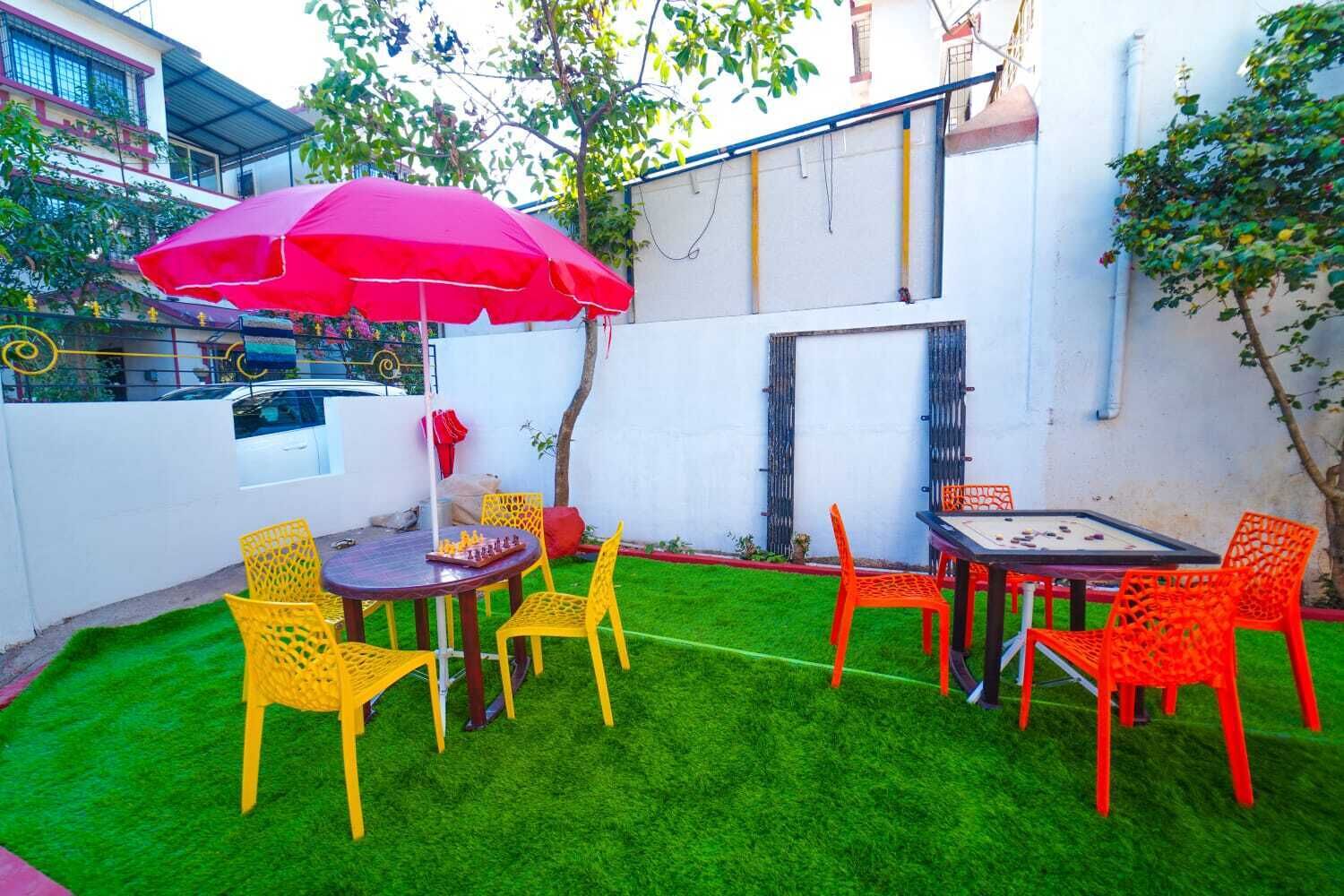 A patio with a chess table, yellow and red chairs, a red umbrella, and a green lawn.
