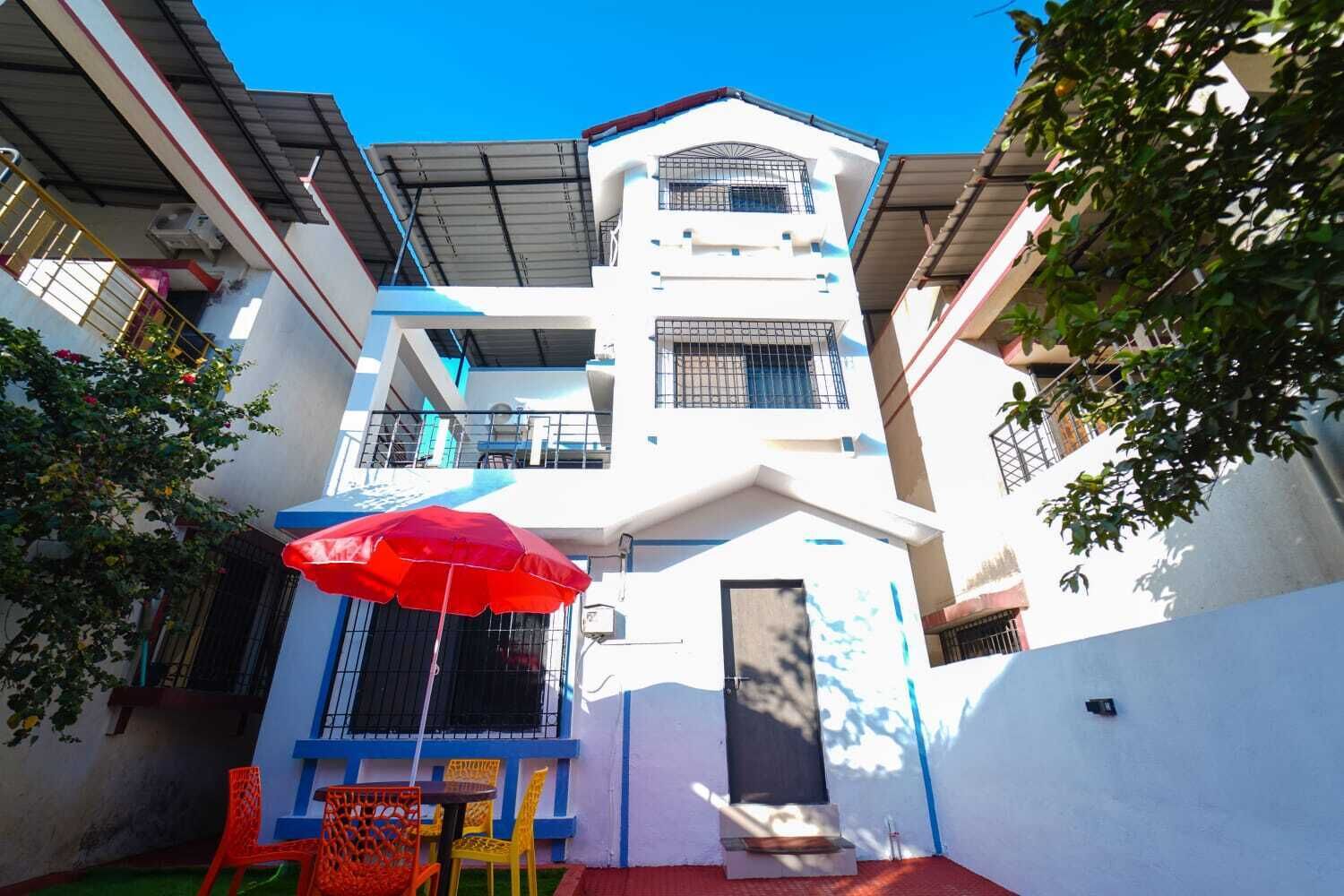 Un edificio de varios pisos con balcones, un paraguas rojo y mobiliario exterior.