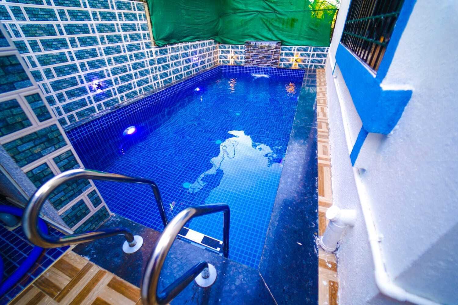 A swimming pool with blue tiles, a metal ladder, and a green tarp.