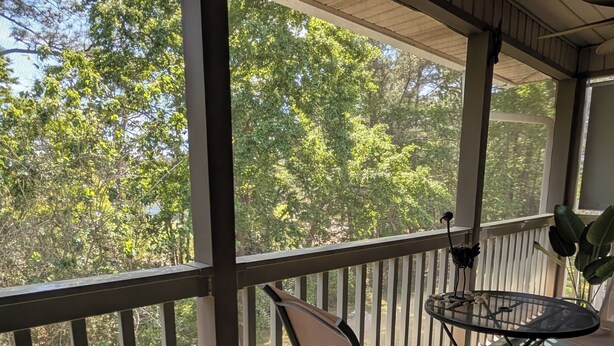 Un espacio al aire libre cubierto con una mesa, sillas, barandilla y vistas a árboles.