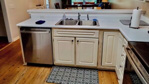Una cocina con lavavajillas, pileta doble, armarios blancos y estufa.