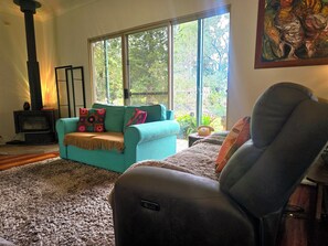 A living room with a sofa, a chair, a fireplace, and a large window with a view of trees.