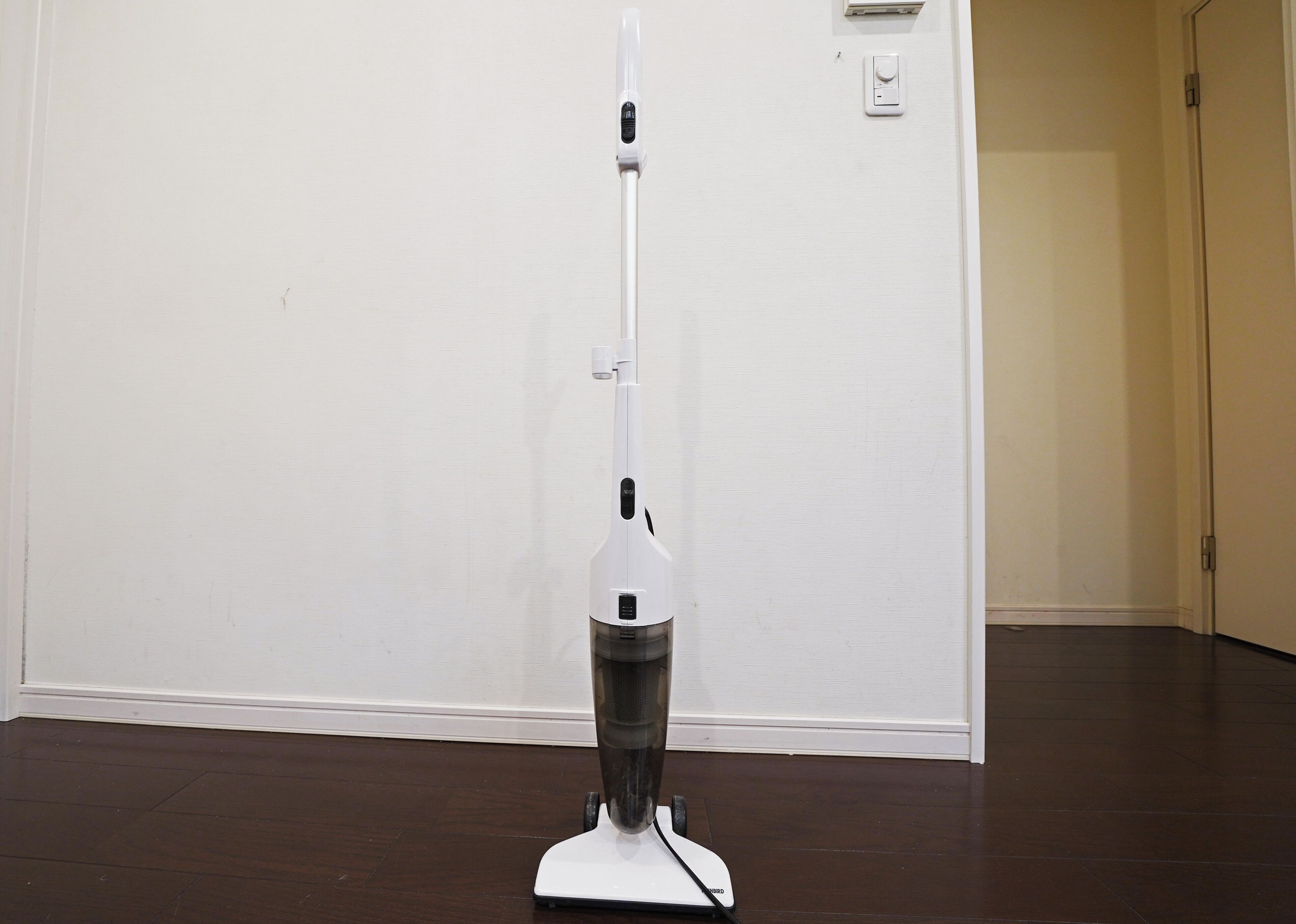 A white upright vacuum cleaner in a room with a wooden floor and a white door.