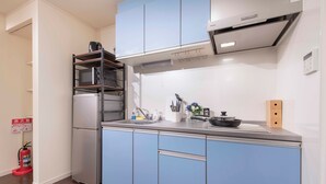 A kitchen with a stainless steel refrigerator, a microwave, a sink, and a wooden block on the counter. - Asakusa The Apartment (Tokyo)