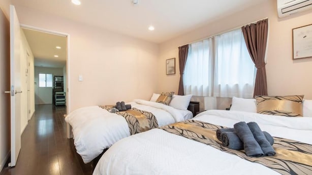 A hotel room with two beds, a hallway, and a door leading to another room. - Asakusa The Apartment (Tokyo)