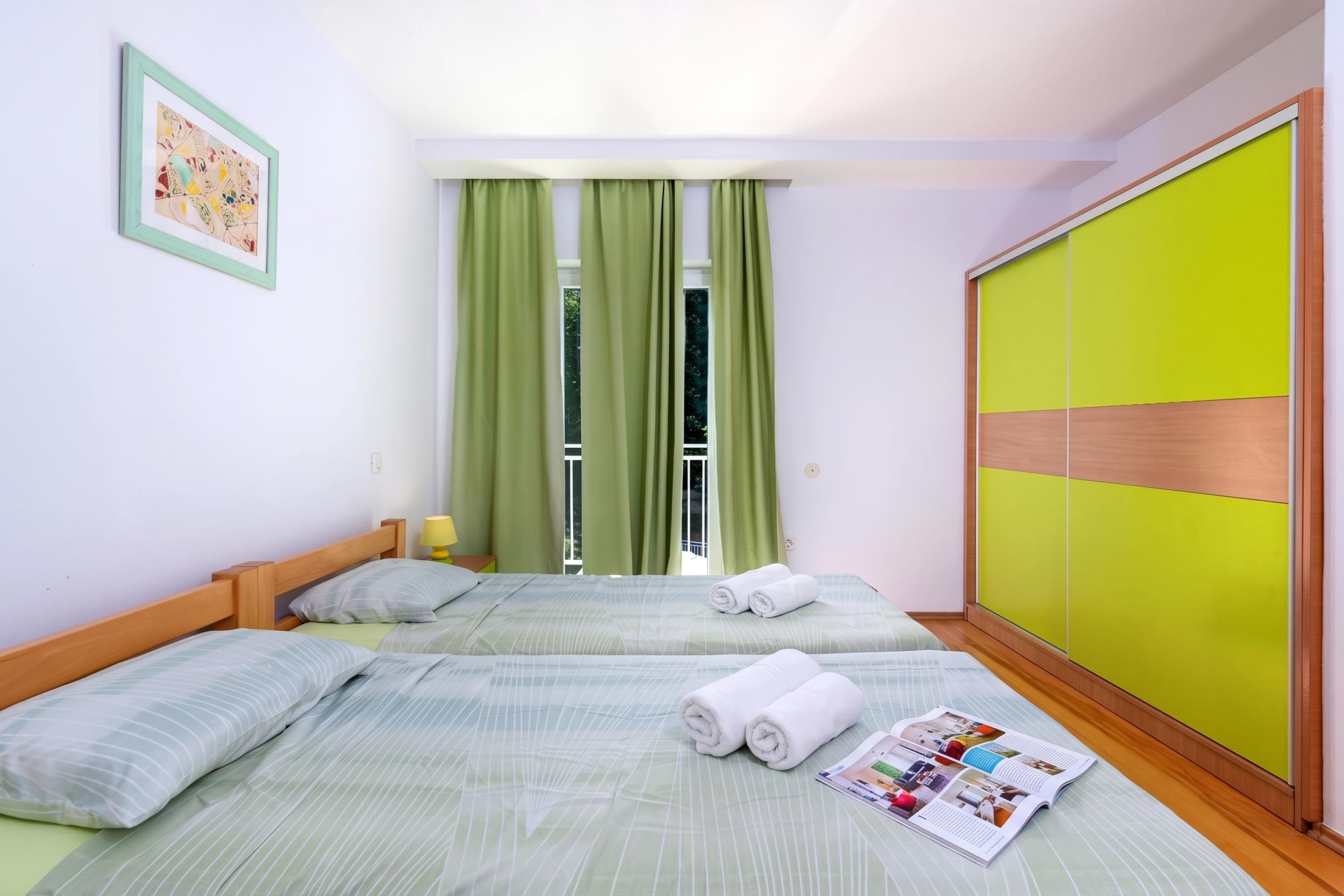 Una habitación de hotel con dos camas, una cortina verde, un cuadro enmarcado y una revista en el suelo.