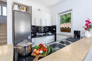 A modern kitchen with stainless steel appliances, a wooden cutting board with vegetables, and a window with a view of greenery. - Villa Ester - Private Pool Escape for 8 (Krsan)