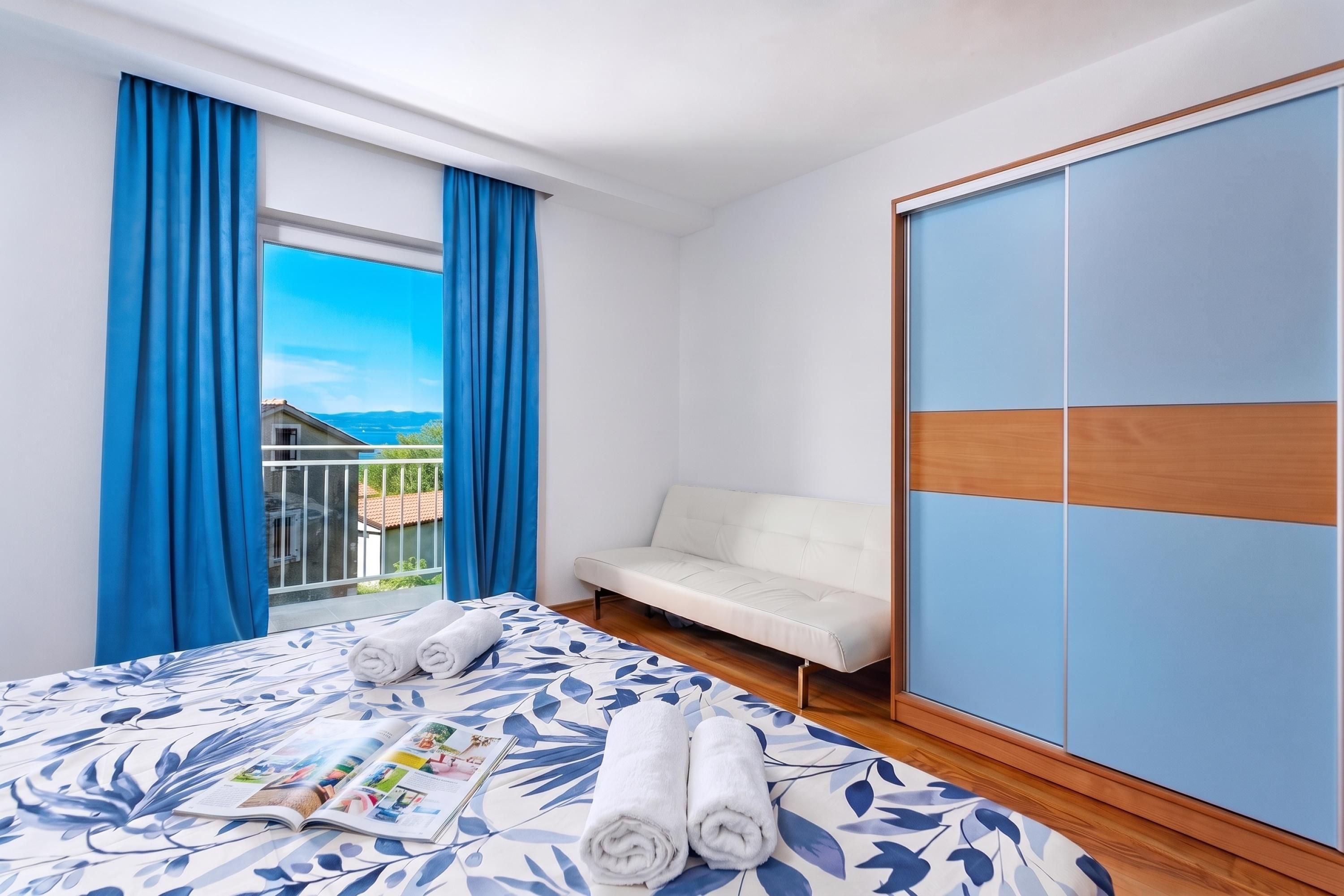 A hotel room with a bed, a sofa, a wardrobe, and a window with curtains.