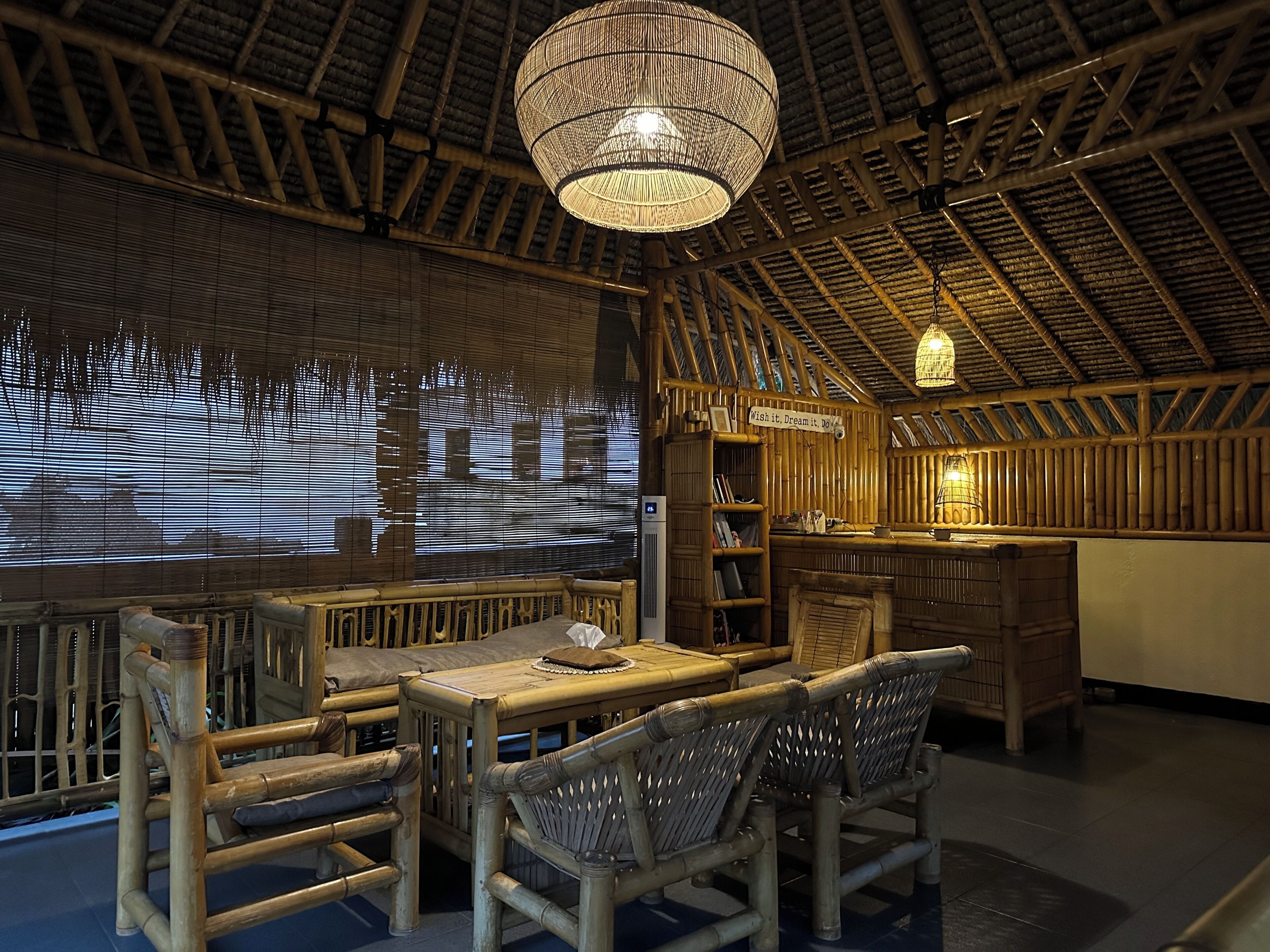 A bamboo-themed restaurant interior with a high ceiling, woven light fixture, and a projection screen displaying a cityscape.
