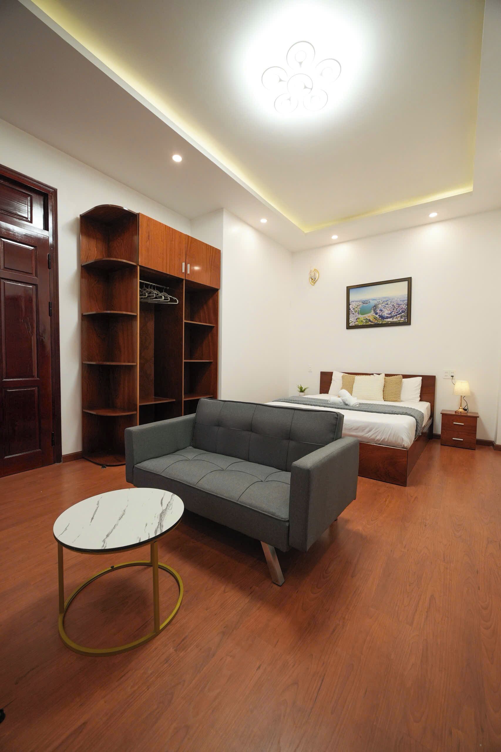 Un dormitorio con una cama, un sofá gris, un armario de madera, una mesa redonda y una lámpara de techo.