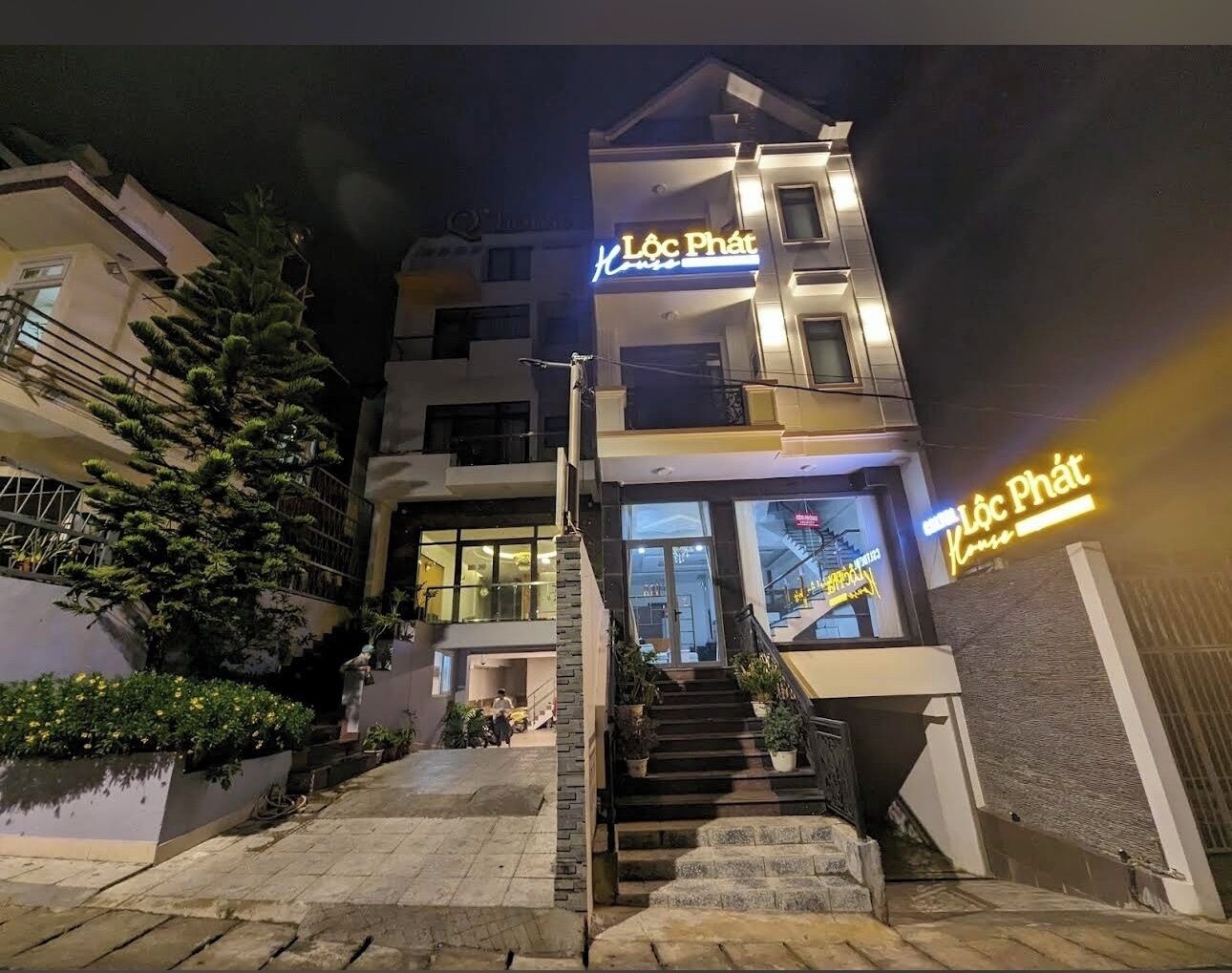 Un immeuble à plusieurs étages, avec un escalier menant à l’entrée, une enseigne au néon indiquant « Lôc Phát » et une façade bien éclairée.