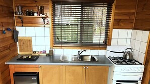 Ett kompakt kök med en inbyggd diskmaskin, en spis, ett handfat och ett fönster med persienner.