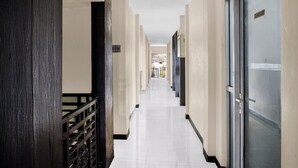 Um corredor com corrimão de madeira, uma porta com aviso e piso de azulejos.