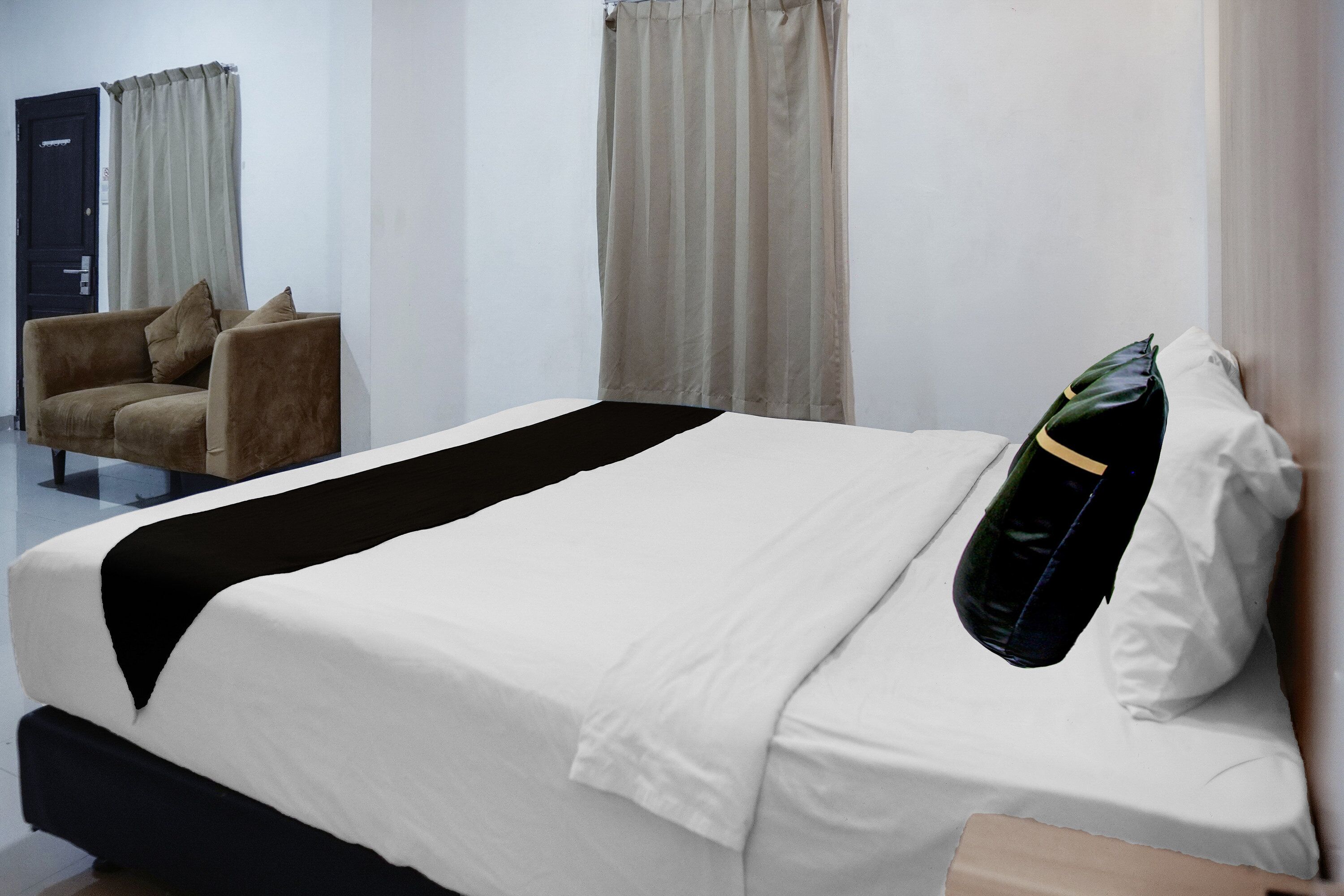 Ett hotellrum med en säng, en stol och gardiner.