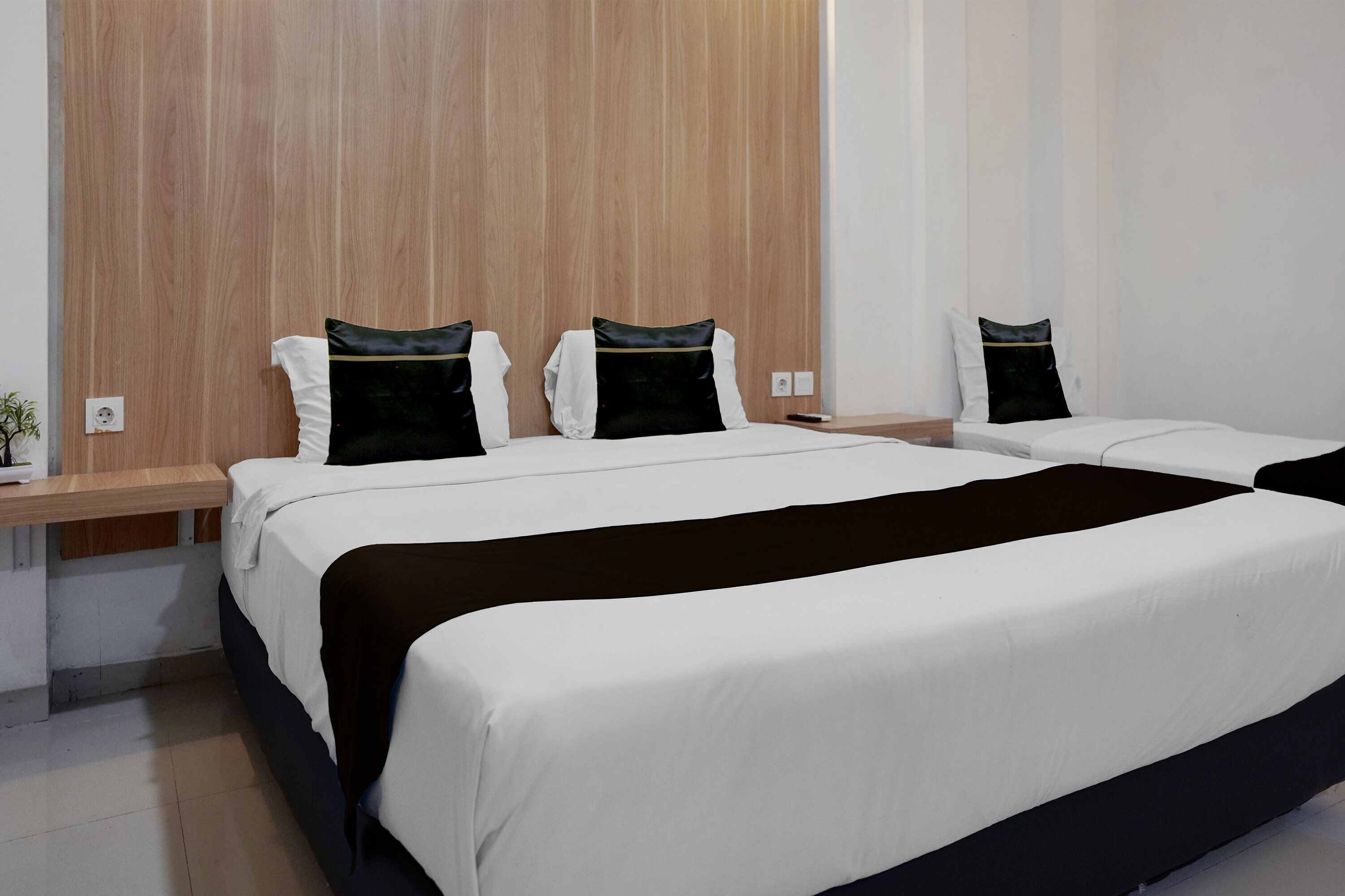 A modern hotel room with a large bed, wooden headboard, and a bedside table with a lamp.