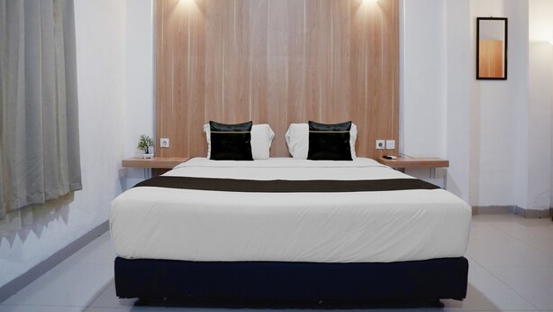 Quarto de hotel com uma cama grande, duas mesas de cabeceira, uma luminária fixada na parede e um espelho.
