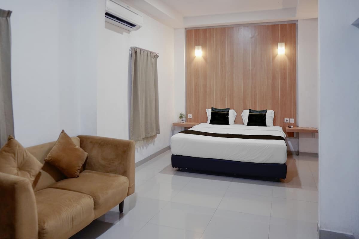 Une chambre d’hôtel comprenant un lit, un canapé, un mur décoratif en bois et une table de chevet avec une lampe.