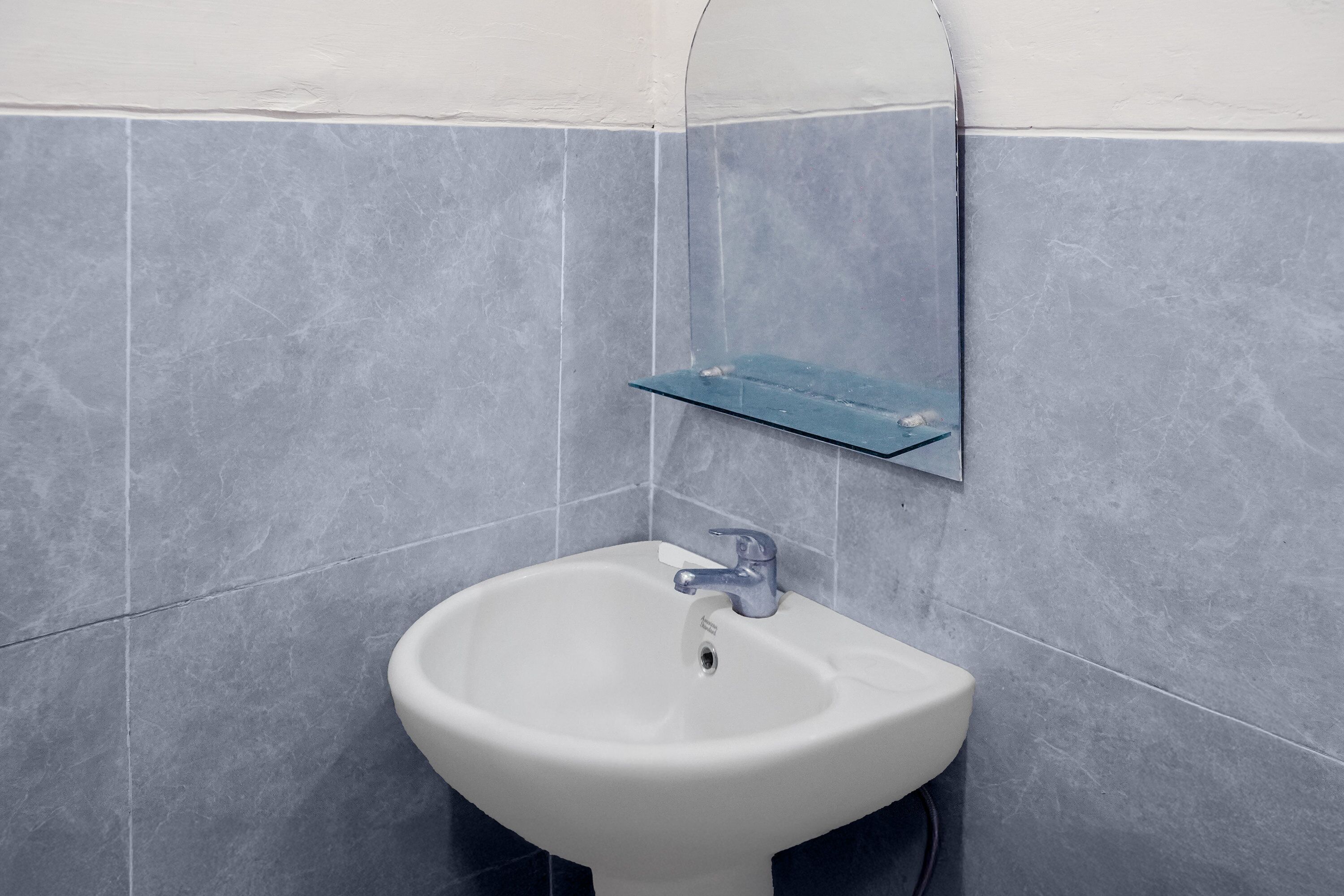 Un baño con un lavamanos blanco, un espejo y un estante azul.