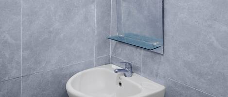 Un baño con un lavamanos blanco, un espejo y un estante azul.