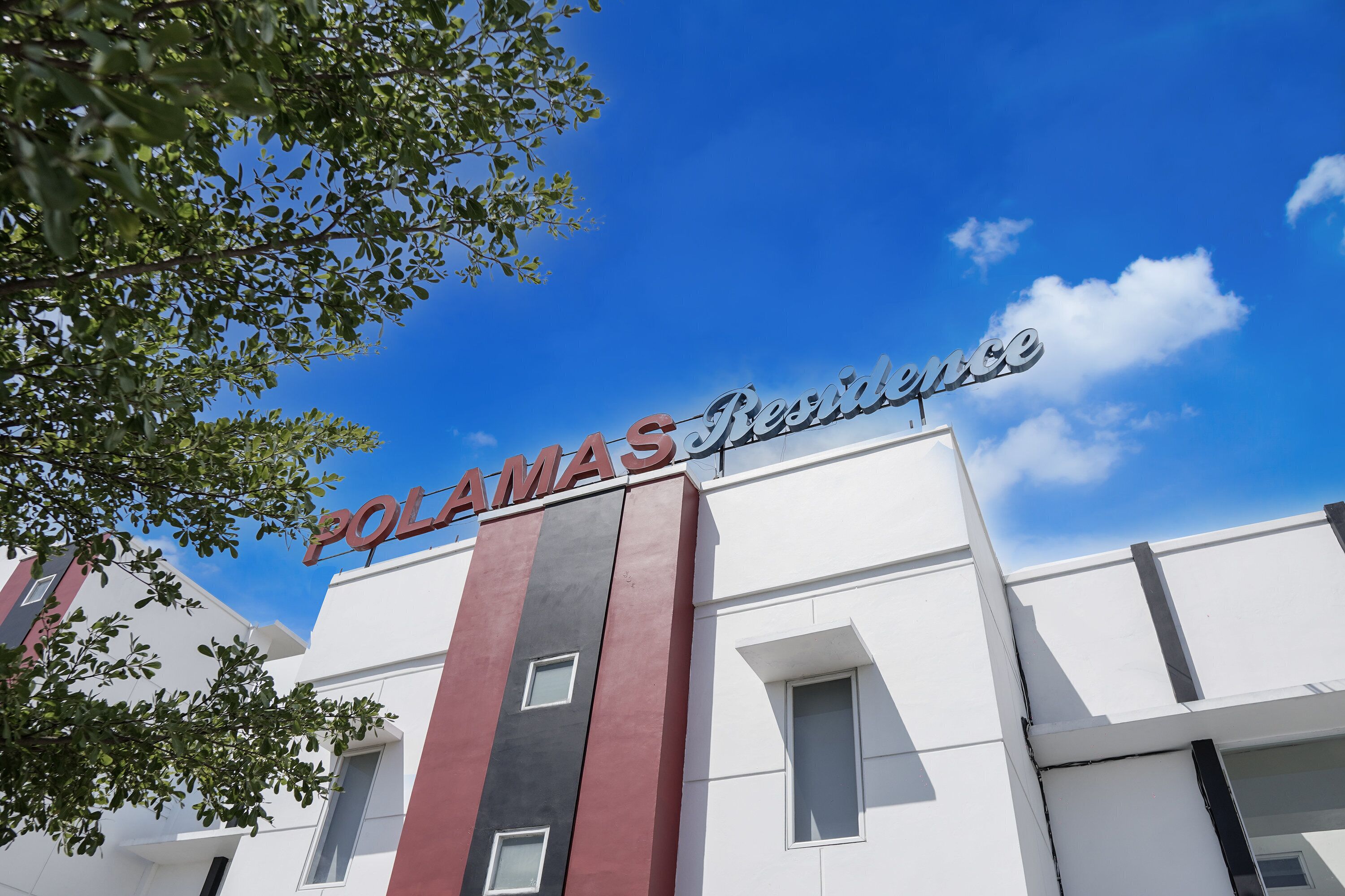 Un immeuble portant l’inscription « POLAMAS Residences », caractérisé par une architecture moderne avec un toit plat et des fenêtres rectangulaires.