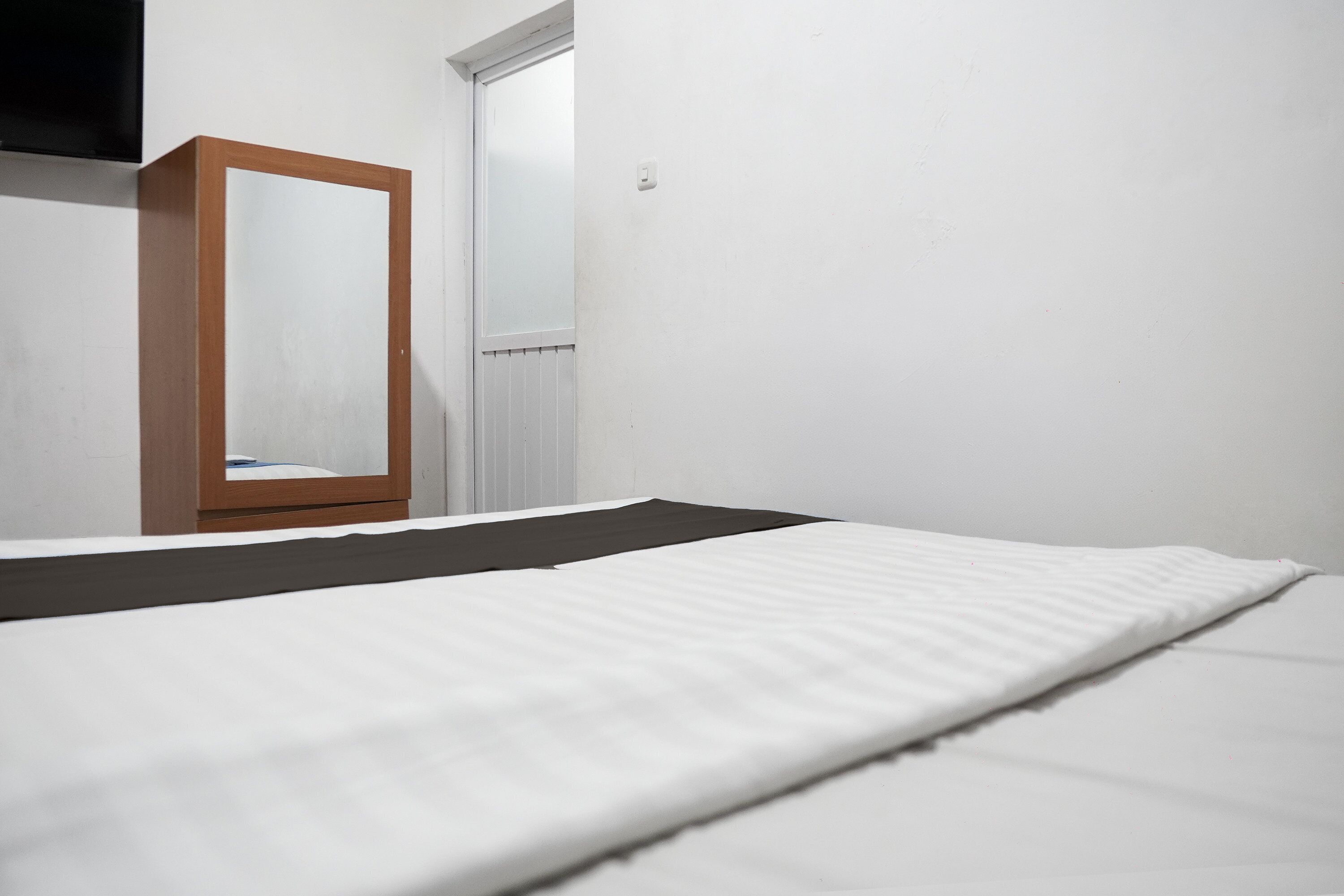 Een kamer met een bed, een spiegel met houten frame en een witte deur.