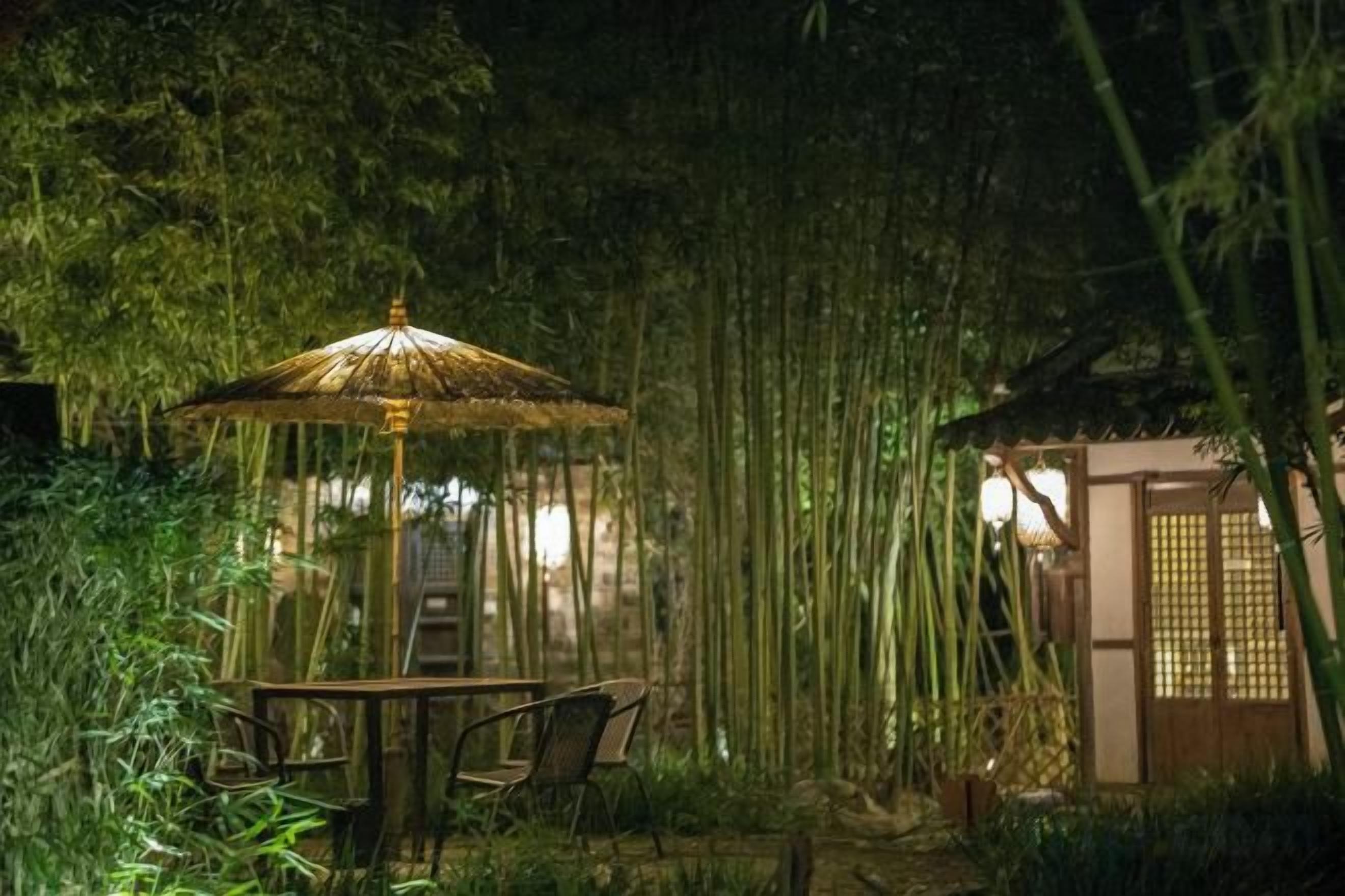 A bamboo forest with a traditional Japanese-style gazebo and a table with chairs.