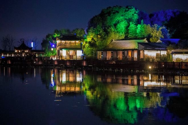 A traditional building with a reflection in the water, surrounded by trees and other structures.