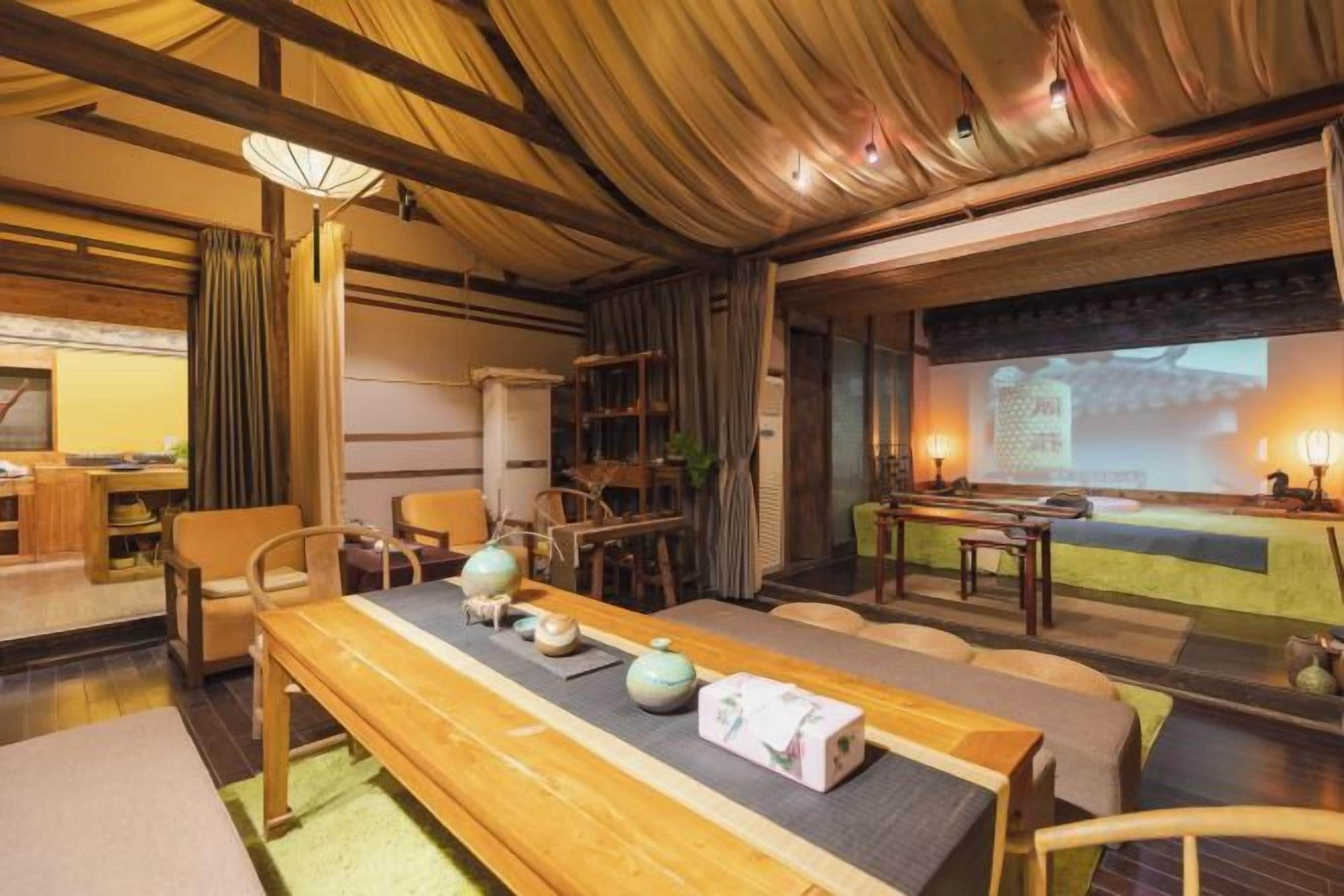A traditional Japanese-style room with tatami flooring, a low table with tea set, and a projection screen displaying a traditional scene.