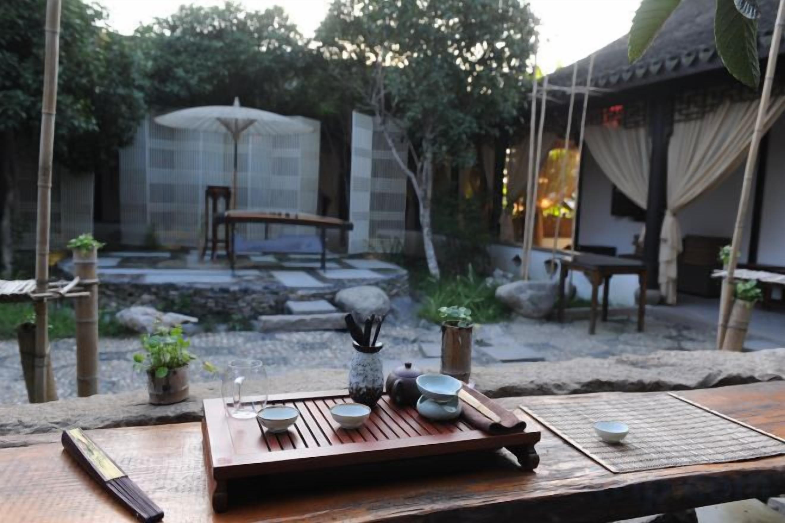 A traditional Japanese tea setting with a wooden table, tea set, and a stone garden in the background.